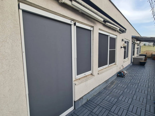 Un toldo vertical en el exterior de varias ventanas y una puerta de patio protege del sol y del calor la fachada de la casa.